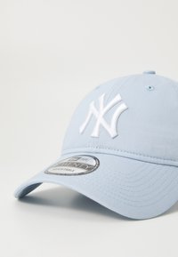 Light blue adjustable baseball cap featuring white embroidered logo, curved brim, and textured fabric with ventilation holes.