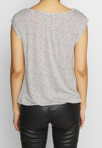 Blouse à manches courtes en tissu léger et à pois. Couleur : blanc avec des pois noirs. Coupe décontractée à l'arrière avec un détail de fronces subtil.