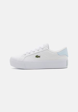 Biały niski sneaker z grubą podeszwą, jasnoniebieskim akcentem na pięcie, białymi sznurowadłami i małym zielonym logo krokodyla z boku.