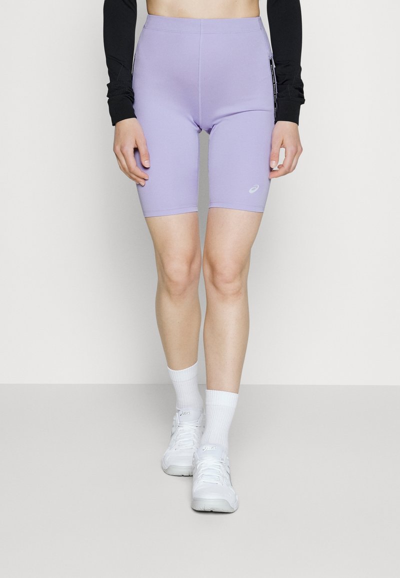 Lavendelkleurige fietsbroeken met een hoge taille, een gladde stof en zijzakken. Gepaard met witte sportschoenen en korte sokken.