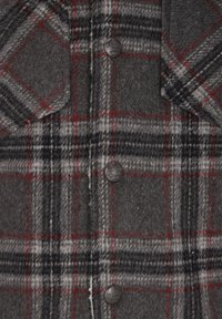 Camisa de cuadros gris con textura de lana, patrones de cuadros en negro y rojo, y botones plateados en la parte frontal y el bolsillo del pecho.