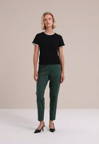 Melnas īsām piedurknēm krekls ar baltu apdari, savienots ar zaļām pieguļošām biksēm un melniem šahtētiem papēžiem. Vienkāršs, moderns dizains, gluda tekstūra.