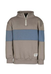 Tostadfärgad och blå färgblockerad pullover-tröja med halv dragkedja och ribbade muddar, nederkant och krage, med en etikett nära nederkanten.