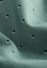 Light green woven fabric with small dark blue and white circular embroidered dots scattered across its textured surface.