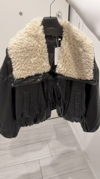 Black leather bomber jacket with a cream faux fur collar, featuring a zipper front, two front pockets, and a boxy design.