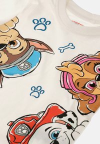 Three cartoon dog faces wearing colorful collars and helmets with paw prints and a small bone on a white fabric background.