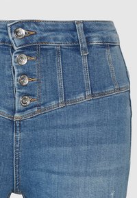 Jeans de denim azul de cintura alta com quatro botões de pressão prateados, detalhes de costura intrincados e uma textura suave, apresentam um design clássico de cinco bolsos.