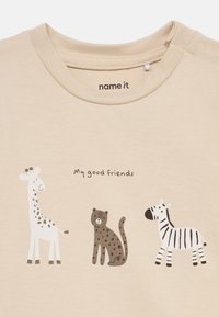 Μπεζ βαμβακερό μπλουζάκι με τρεις ζωγραφιές ζώων: μια καμηλοπάρδαλη, ένα λεοπάρδαλη και μια ζέβρα, με το κείμενο "Οι καλοί μου φίλοι" από κάτω.