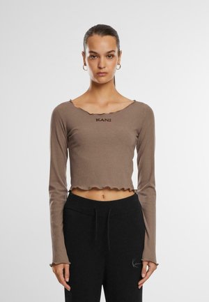 Brun ribbet langermet cropped topp med bølgede kanter og logodetalj. Kombinert med svarte joggebukser med snor og logoaksent.