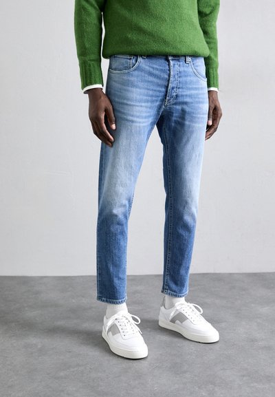 Jeans din denim de culoare albastră deschisă, cu o croială dreaptă, având buzunare frontale și un finisaj decolorat, asortați cu adidași albi și un pulover verde.