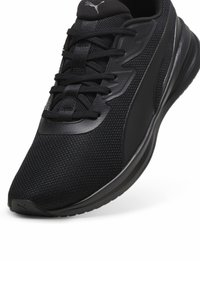 Zapato deportivo negro con parte superior de malla texturizada, suela de goma, cordones y un panel de acento liso en el lado. Presenta un logo en el talón.