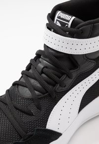 Baskets montantes Puma noires et blanches avec lacets, sangle perforée blanche, dessus en mesh et cuir, et logo de la marque sur la languette.