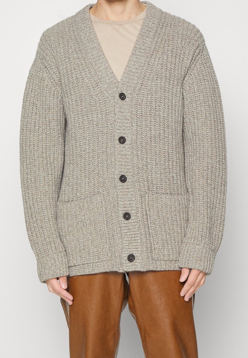 Grå stickad kofta med V-ringning, fyra svarta knappar, två framfickor och ribbade ärmslut och fåll. Standard passform med textilmaterial.