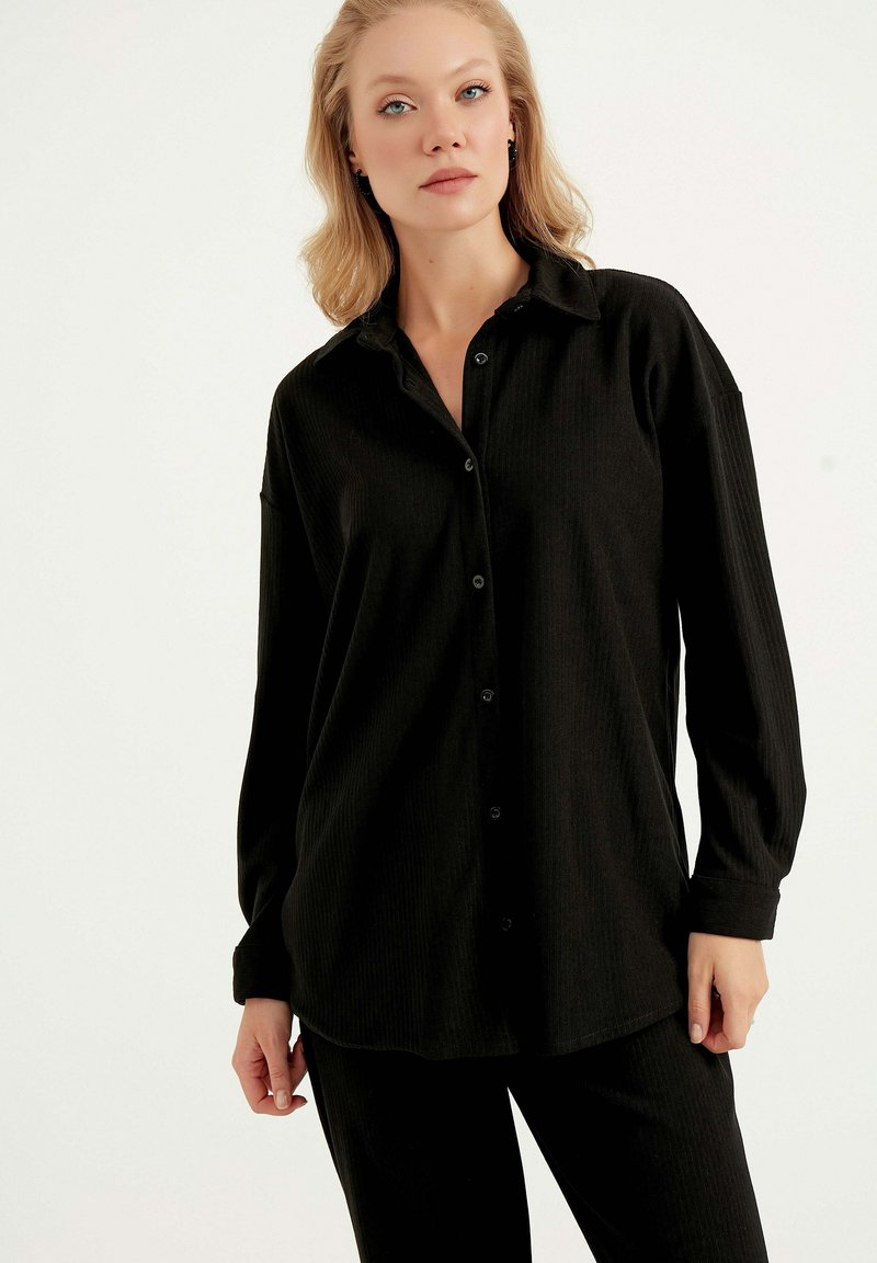 Schwarzes Hemd mit Knöpfen und Kragen, langen Ärmeln und gerippter Textur. Der Stoff ist leicht und hat einen leicht lockeren Schnitt.