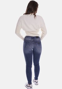 Maglione bianco morbido a maglia con scollatura rotonda, abbinato a jeans skinny blu scuro con due tasche posteriori e un piccolo etichetta nera.