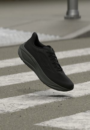 Chaussure de course noire à semelle épaisse suspendue au-dessus d'un passage piéton dans une rue urbaine, avec de petits débris éparpillés en dessous.