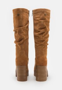 Bottes hautes marron en daim avec un design décontracté, dotées d'un talon épais et de deux fermetures éclair à l'arrière. Texture lisse et forme structurée.