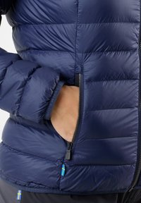 Navy puffer jacket with quilted texture, zipper pocket, and contrast blue and yellow flag detail. Fabric appears lightweight and water-resistant.