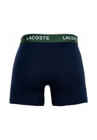 Boxer da uomo blu navy con cintura elastica verde e logo "LACOSTE" bianco. Materiale in cotone morbido, lunghezza a metà coscia.