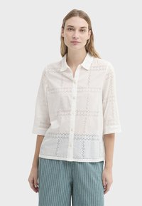 Chemise en coton blanc avec broderie ajourée en motif quadrillé, col, boutonnage sur le devant et manches trois-quarts.
