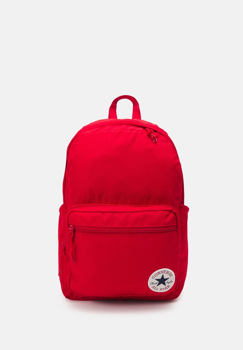 Sac à dos rouge vif avec poche zippée à l'avant et écusson du logo Converse All Star sur un fond clair uni.