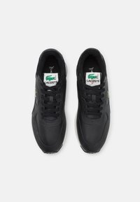 Baskets noires avec une tige en cuir lisse, comprenant un bout arrondi, un design à lacets et deux étiquettes de logo Lacoste sur la languette.