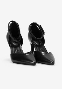 Zapatos de tacón alto negros con un diseño de punta afilada, tira de tobillo y textura de cuero suave. Presentan una silueta elegante y acentos minimalistas.