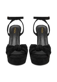 Černé platformní podpatky s uzlovým detailem vpředu, vyrobené z semišového materiálu, otevřená špička a pásek kolem kotníku. Lesklá černá stélka s logem.
