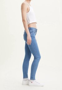 Jeans ajustados de mezclilla de color azul claro. Cuentan con una cintura de altura media y bolsillos traseros con costuras distintivas. Combinados con zapatillas blancas.