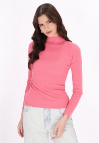 Pulover roz cu guler înalt și mâneci lungi, cu un design fit. Asortat cu pantaloni din denim deschis, având o textură moale și un finisaj neted.
