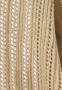 Beige neulekangas, jossa on pitsikuvio ja pystysuorat raidoitukset sekä avoimet kudokset, luoden tekstuuriltaan mielenkiintoisen ilmeen.