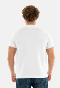 T-shirt bianca a maniche corte vista da dietro, realizzata in cotone, con collo rotondo e finitura pulita. Abbinata a jeans in denim blu.