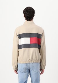 Beige jakke med et fargeblokkdesign i marineblått, hvitt og rødt over ryggen. Elastiske mansjetter og kant. Uformelt, lett materiale.