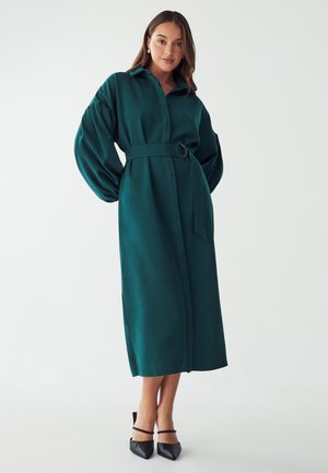 Long green coat made of soft fabric, featuring a collared neckline, puffed sleeves, a belted waist, and a mid-calf length design.