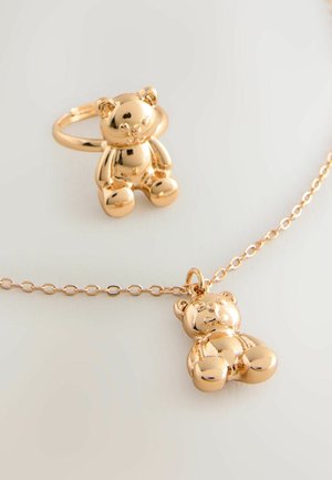 Zlatý šperk set s pendantom vo forme medvedíka na retiazke a zodpovedajúcim prsteňom, oboje s lesklou, hladkou textúrou.