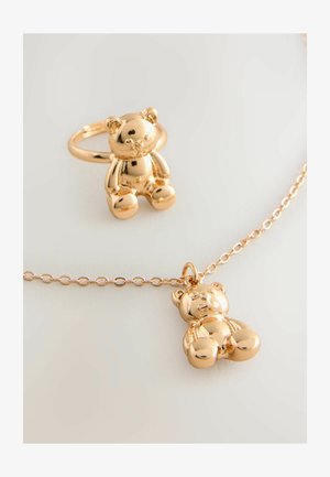 Zelta tonī veidota rotu komplekta, kas sastāv no lācīša piekariņa uz ķēdes un atbilstošas gredzena, abiem ar spīguļojošu, gludu tekstūru.