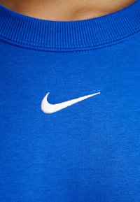 Blå bomullscollege med en vit broderad Nike-logotyp på bröstet. Halslinningen är ribbad för extra textur.