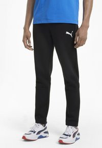 Zwarte sportleggings met een getailleerd ontwerp en een wit Puma-logo op de linker dij, gecombineerd met witte en blauwe sneakers.