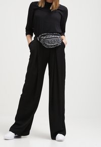 Top nero e pantaloni neri a gamba larga, abbinati a un marsupio a strisce in bianco e nero. Le sneakers bianche completano il look.