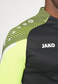 Kurzärmliges Sportshirt in Schwarz und Neon Grün, mit gestreiftem Muster, rundem Logo-Detail und weißen Akzenten an der Schulter.