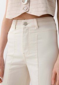 Hoge taille, crèmekleurige jeans met een zachte textuur, voorzien van een zilveren knoopsluiting en opvallende voorzakken.