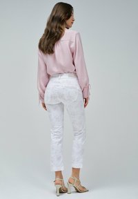 Pantalones de flores blancas con cintura alta, combinados con una blusa de color rosa claro. El conjunto se completa con tacones de tiras beige.