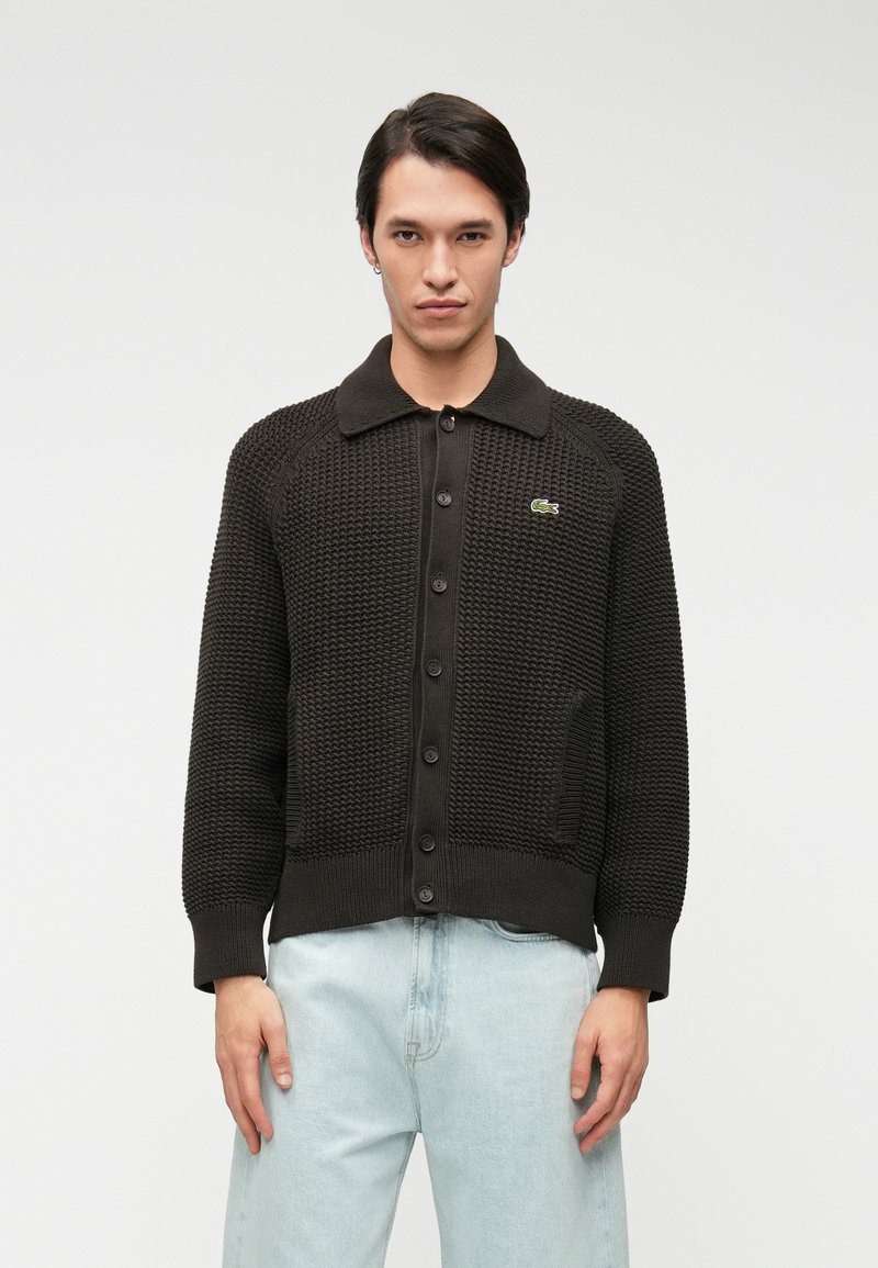 Cardigan noir en tricot avec un motif texturé, des poignets et un ourlet côtelés, avec un col et un devant à bouton, et un petit logo en accent.