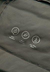 Tessuto idrorepellente, imbottitura in piume d'oca e icone di cerniera facile da chiudere su materiale di giacca verde scuro.