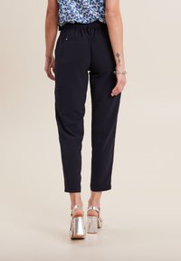 Zwarte, getextureerde broek met een tapse pasvorm en een elastische tailleband, voorzien van zijzakken en een soepele stof. Gemaakt in combinatie met zilveren plateauhakken.