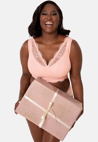 Lace bralette and matching panties in soft pink. She holds a gift, wrapped in glittery pink paper with a cream ribbon.