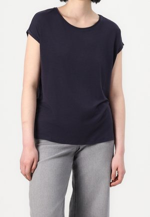 Navyblå t-shirt lavet af blødt bomuldsstof, med korte op rullede ærmer, rund halsudskæring og en afslappet pasform. Sammen med lysegrå bukser med vide ben.