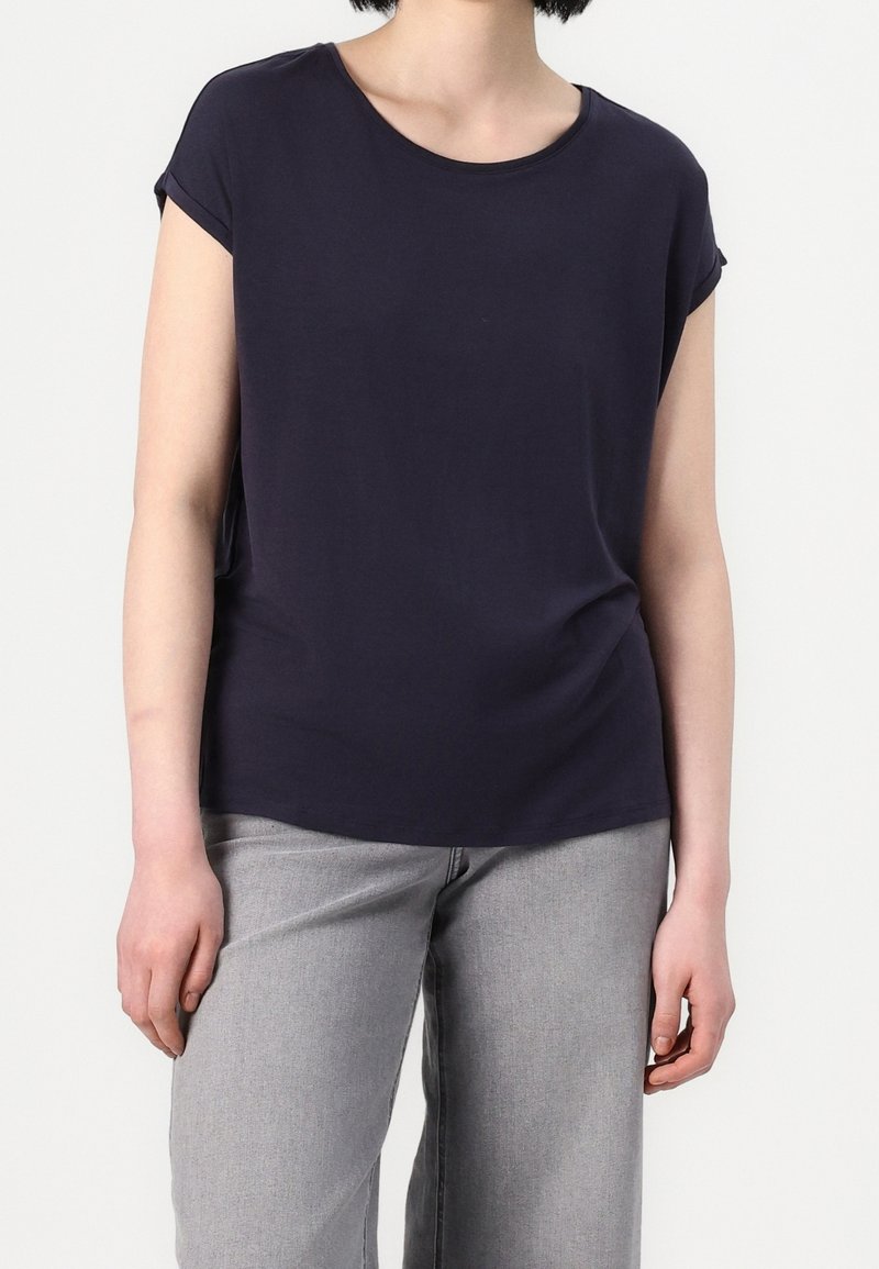 T-shirt bleu marine en coton doux, avec des manches courtes retroussées, un col rond et une coupe décontractée. Associé à un jean gris clair à jambes larges.