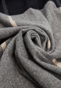 Szary wełniany szalik o fakturowanym splocie, z jasnobeżowymi paskami. Tkanina jest miękka i układa się w spiralny kształt.