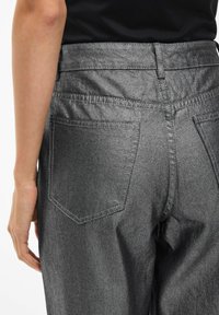 Pantalones de mezclilla grises con una textura suave, que presentan bolsillos traseros y una cintura de altura media, mostrados desde atrás con una mano descansando cerca.